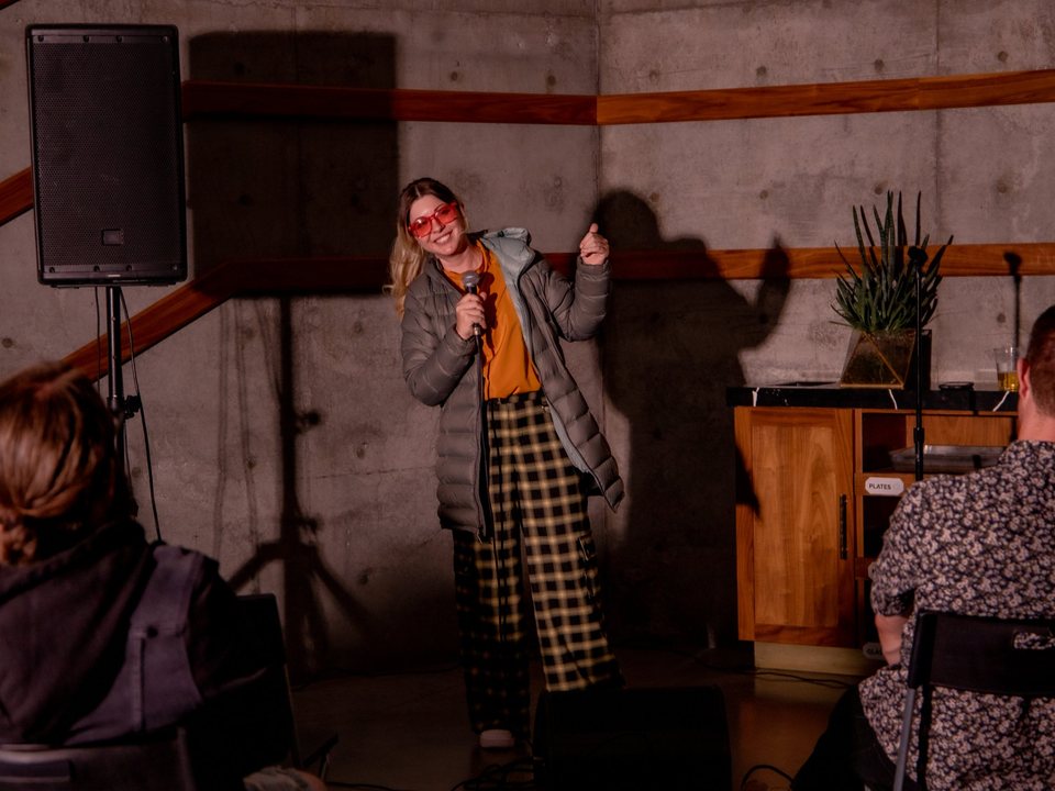 A comedian performs against a concrete wall at Mothership Coffee